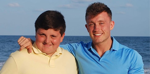 Hemophilia A patient, Zach Mullins, standing with his arm over his brother’s shoulder and the sea behind them